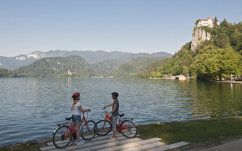 Cyclists by Lake Bled with Bled Castle on a cliff in the background
