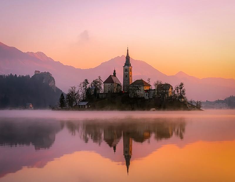 Sunrise view of Lake Bled with the church on Bled Island reflected in calm waters, an iconic Slovenia Alps hiking and cycling destination.