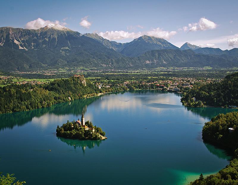 Panoramic view of Lake Bled with its island church, castle and Julian Alps, highlight of cycling and hiking tours.