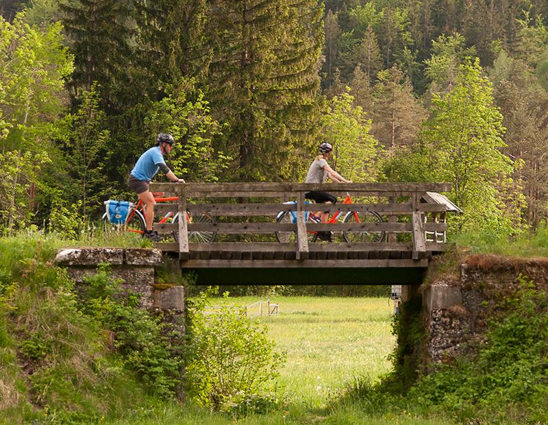 Cyclists riding across a wooden bridge in Slovenia’s countryside during a self-guided cycling holiday.