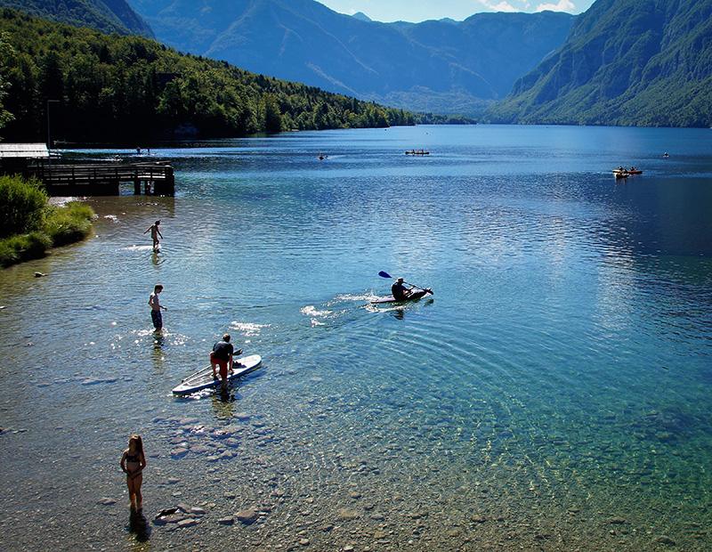 Lake Bohinj in Slovenia with people swimming and paddleboarding, popular destination on self-guided cycling and hiking holidays.