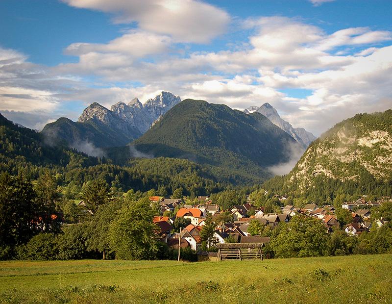 Scenic view over a Slovenian alpine village with mountains in the background, part of self-guided hiking routes in the Julian Alps.
