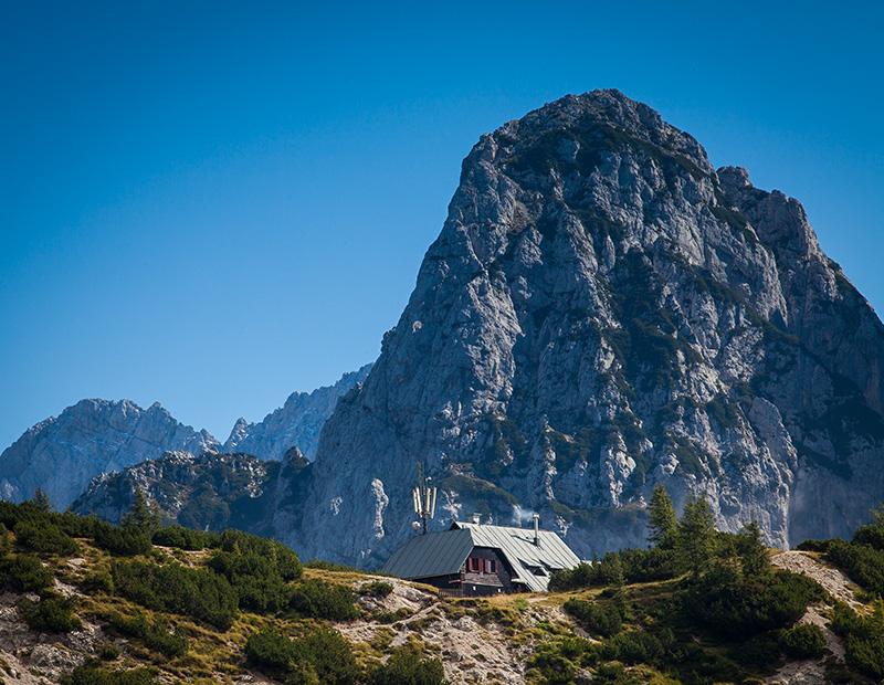 Mountain hut beneath dramatic cliffs in the Julian Alps, Slovenia, resting point for self-guided trekking and hiking tours.