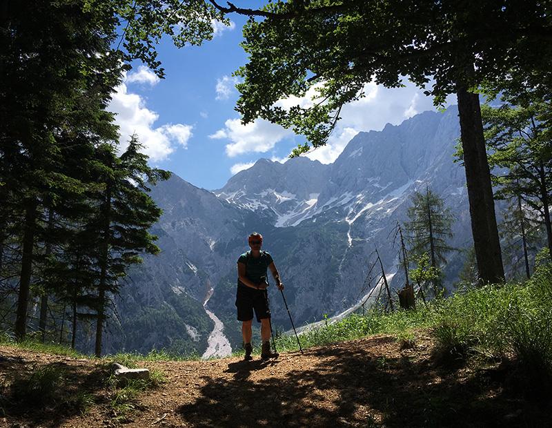 Hiker standing on a forest viewpoint with alpine peaks in the background, enjoying self-guided trekking in Slovenia.