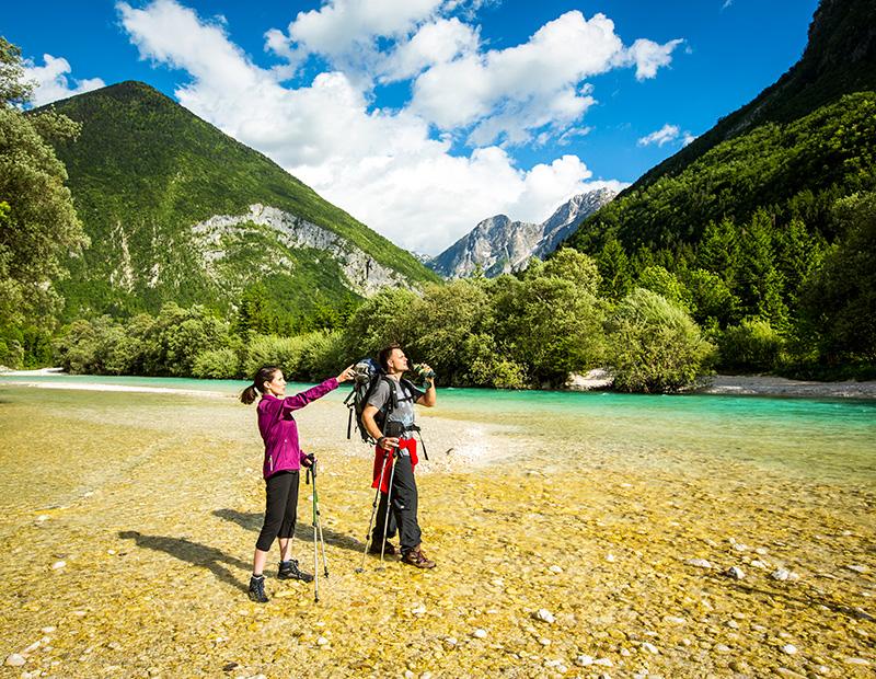 Hikers by the turquoise Soča River in Slovenia, enjoying self-guided walking holidays in the Julian Alps.