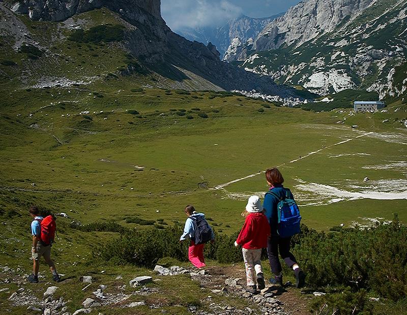 Family of hikers walking across alpine meadows in Slovenia’s Julian Alps, exploring self-guided mountain trekking routes.