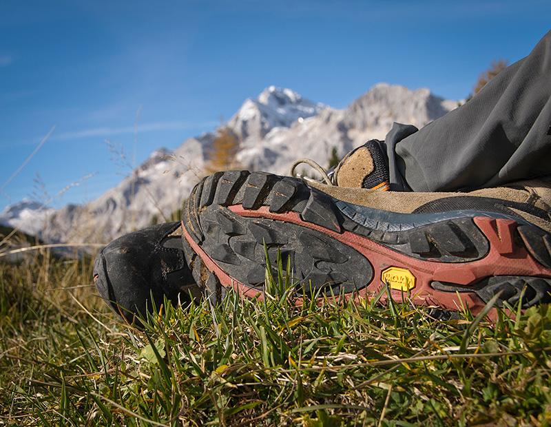 Resting hiker with trekking boots and Julian Alps peaks in the background, enjoying self-guided hiking holiday in Slovenia.