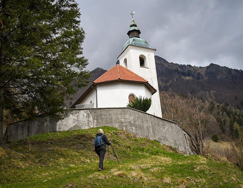 Hiker approaching St. John the Baptist church in Bohinj, Slovenia, cultural highlight on self-guided walking holidays.