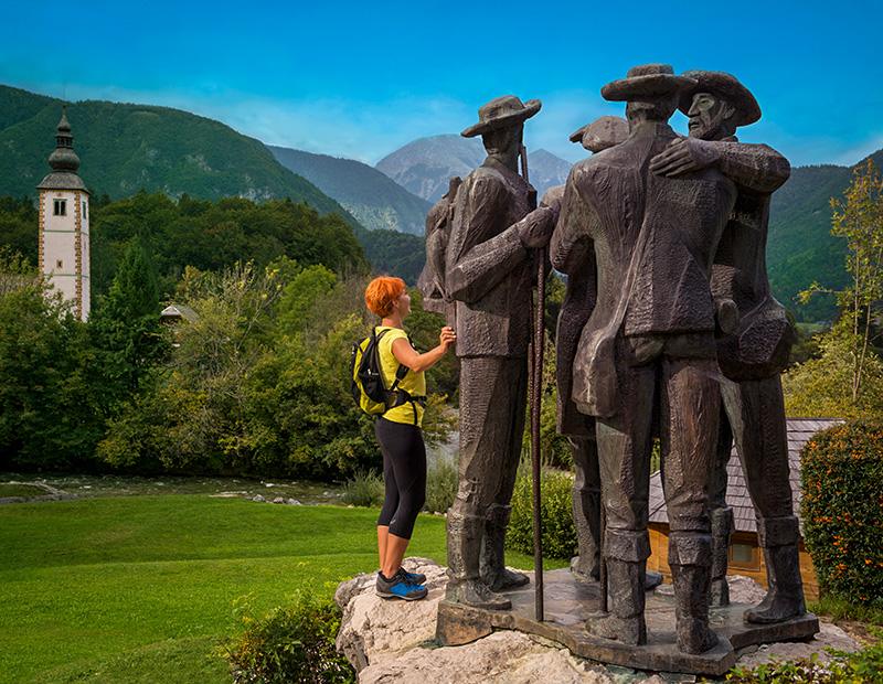 Statue of four hikers in Bohinj, Slovenia, with St. John the Baptist church in the background, celebrating alpine hiking heritage.