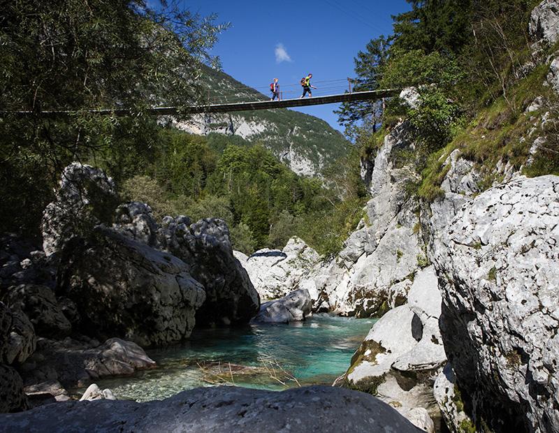 Hikers crossing bridge over turquoise river in the Soča Valley during a self-guided walking holiday in Slovenia.