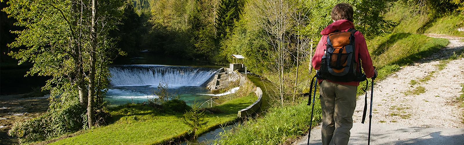 Hiker walking beside a forest stream and small waterfall in Slovenia